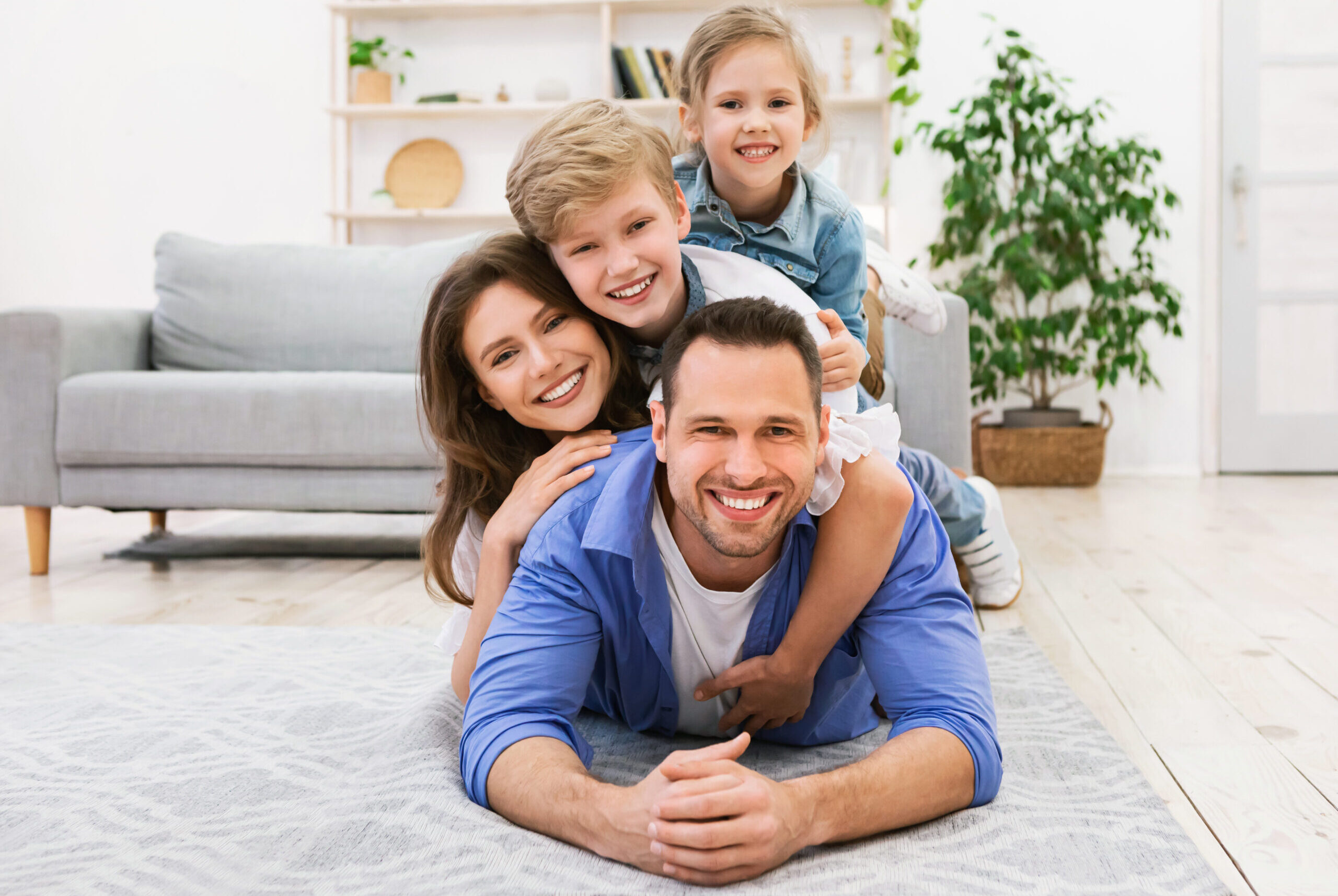 Funny Family Portrait. Happy Parents And Children Posing Lying On Floor Together Looking At Camera At Home. Free Space